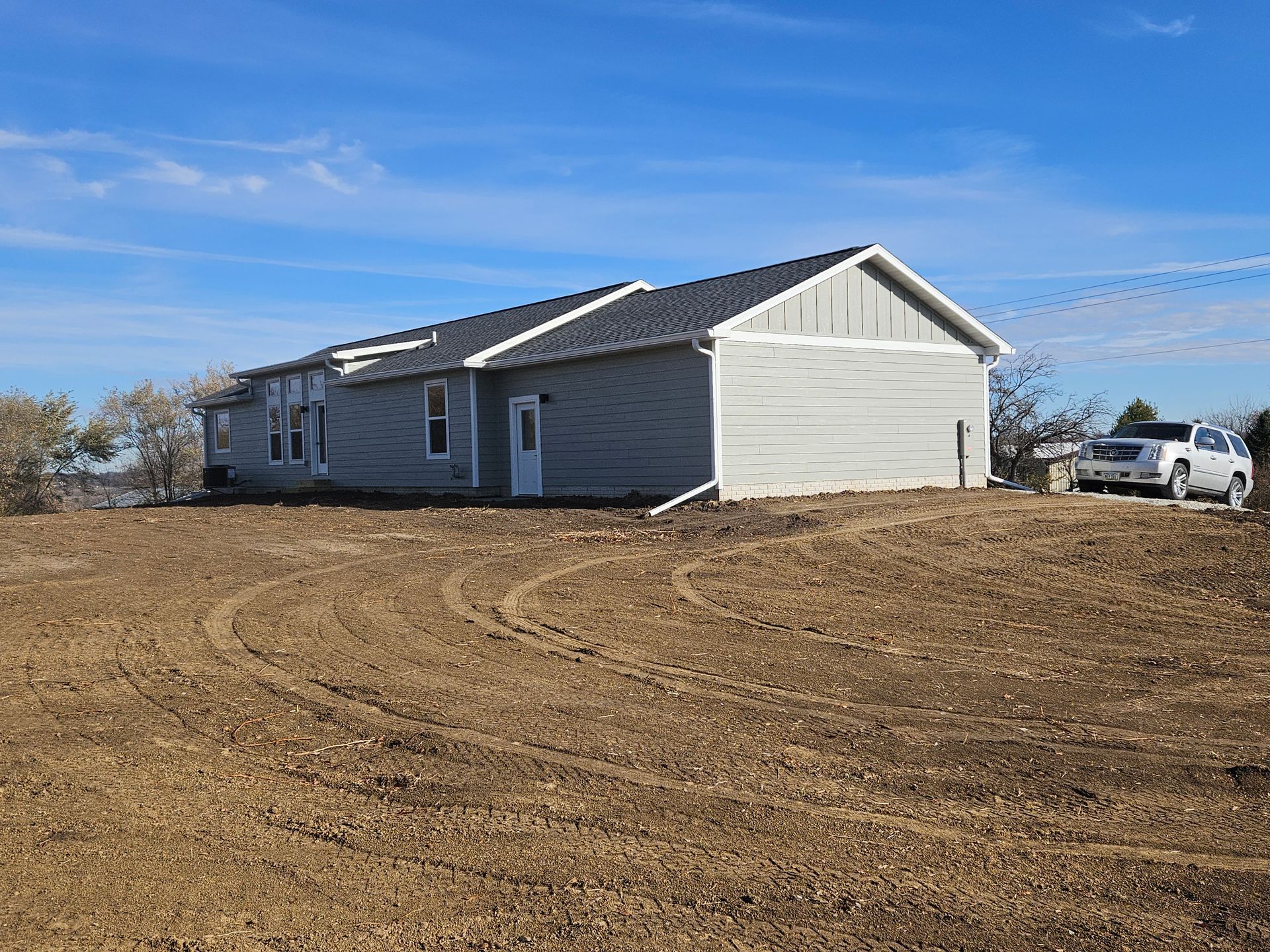 Gray house on a hill with a pickup truck parked nearby against a blue sky.