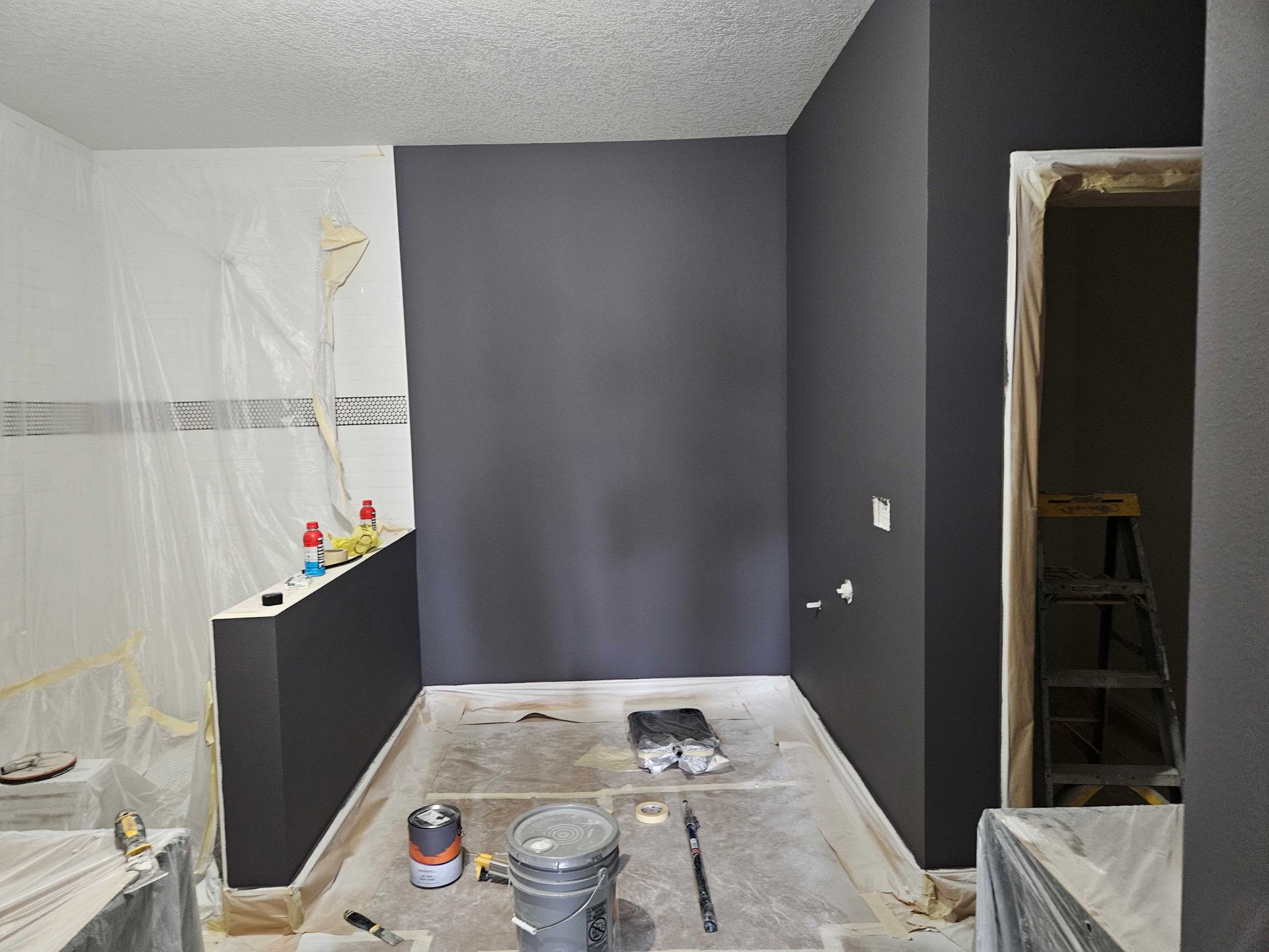 Room partially painted dark gray. Unfinished floor. White ceiling. Plastic covering.