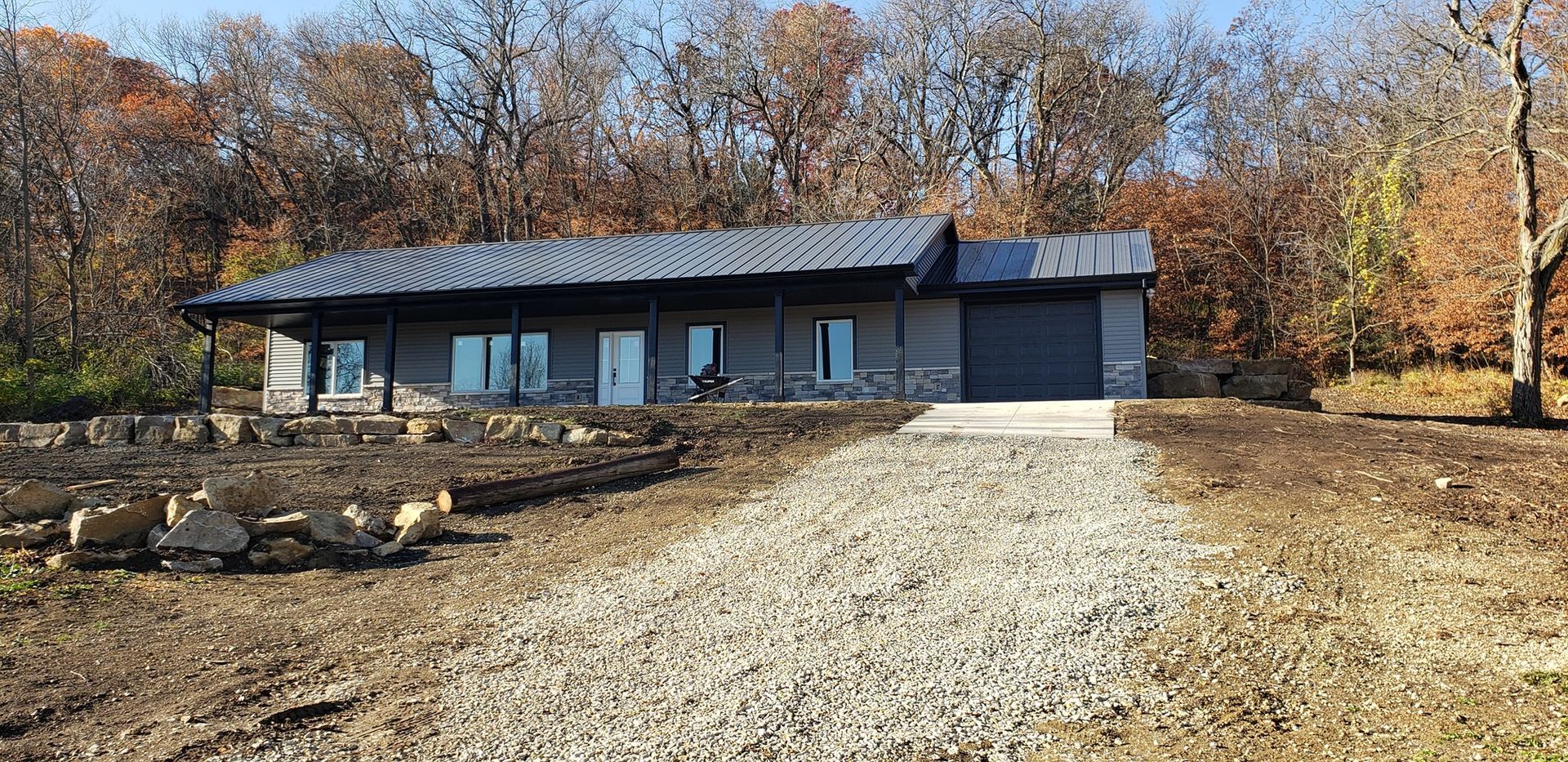 A modern, single-story house with a gravel driveway set in a wooded area.
