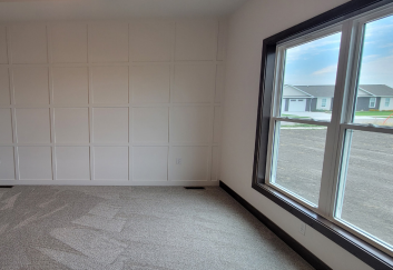 Empty room with carpet, paneled wall, and large window overlooking a residential area with gray sky.