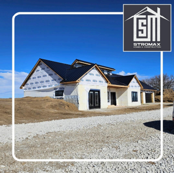 New house under construction with black roof and white wrap, logo in corner.