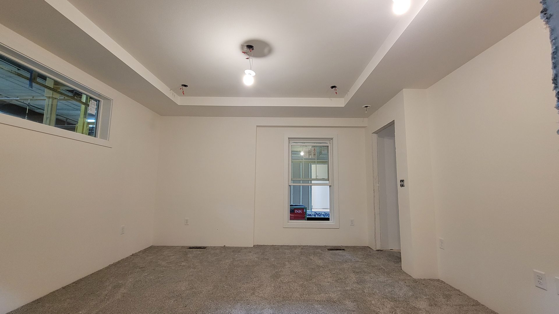 Empty room with white walls, carpeted floor, ceiling lights, and a window.