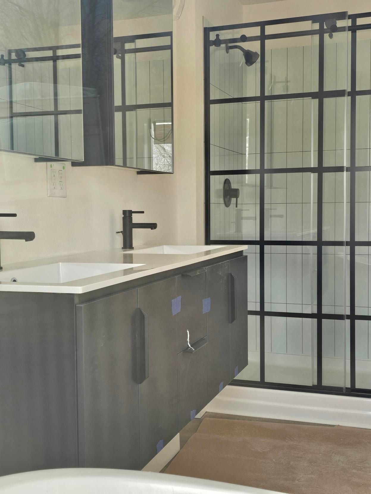 Modern bathroom with black-framed shower and vanity. Dark gray cabinets, white countertop, and fixtures.