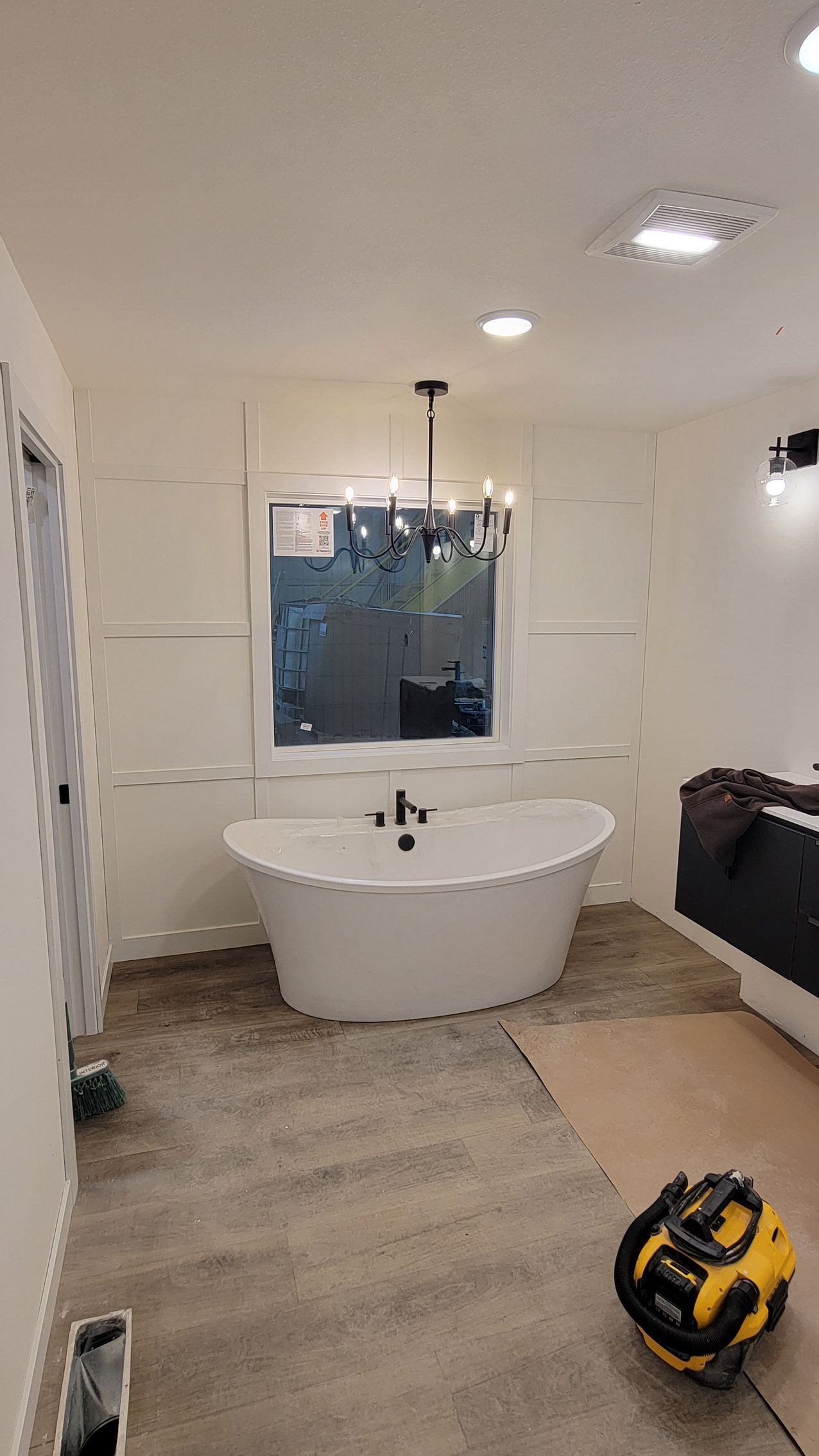 Bathroom with a white freestanding tub under a window. Construction in progress with bare floors and tool.