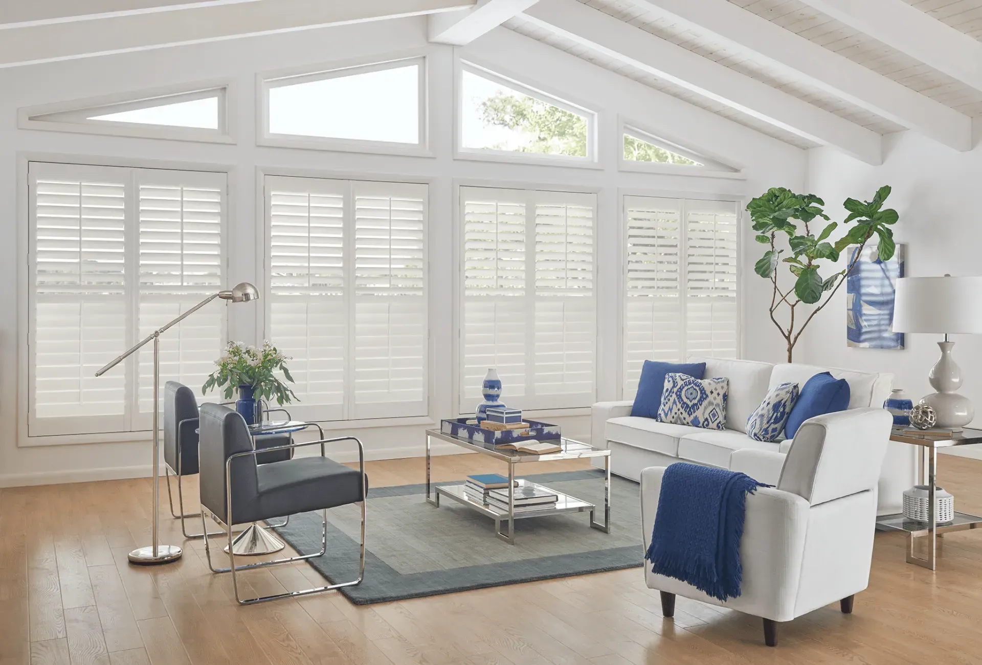 Living room with white walls, shuttered windows, blue and white decor, wood floors.