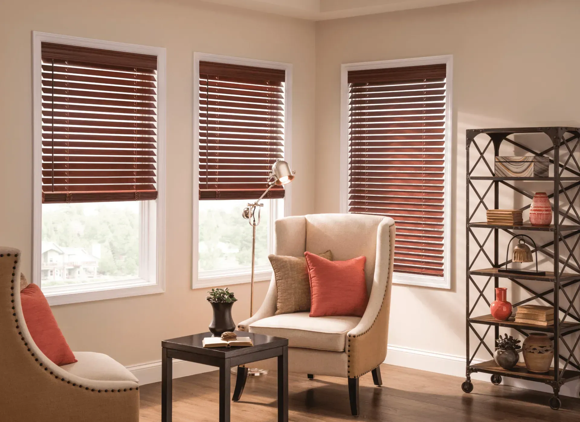 Cozy living room with wooden blinds, neutral walls, cream armchair, and dark brown bookshelf.