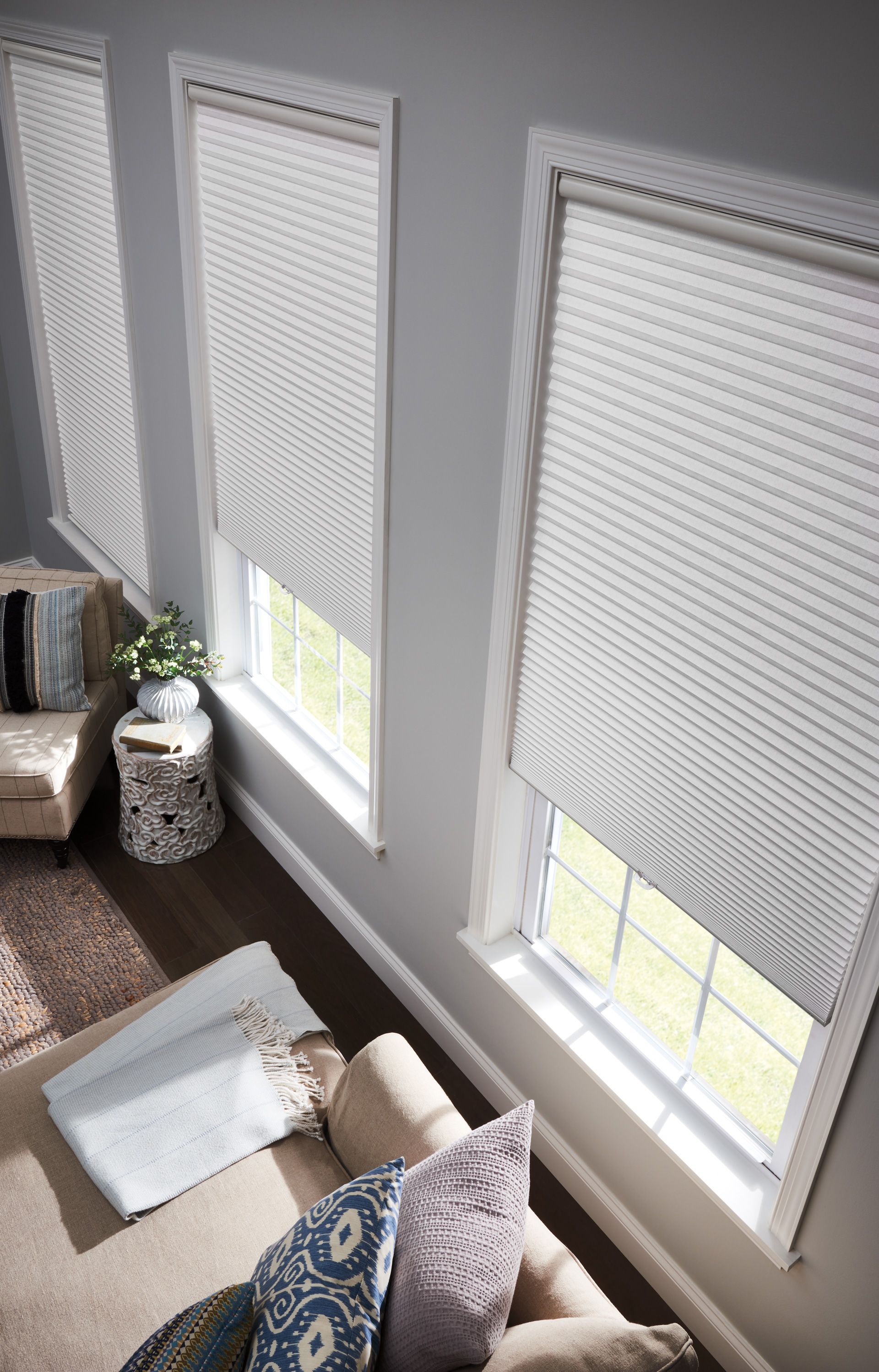 White honeycomb shades on three windows in a living room with a sofa, rug, and side table.
