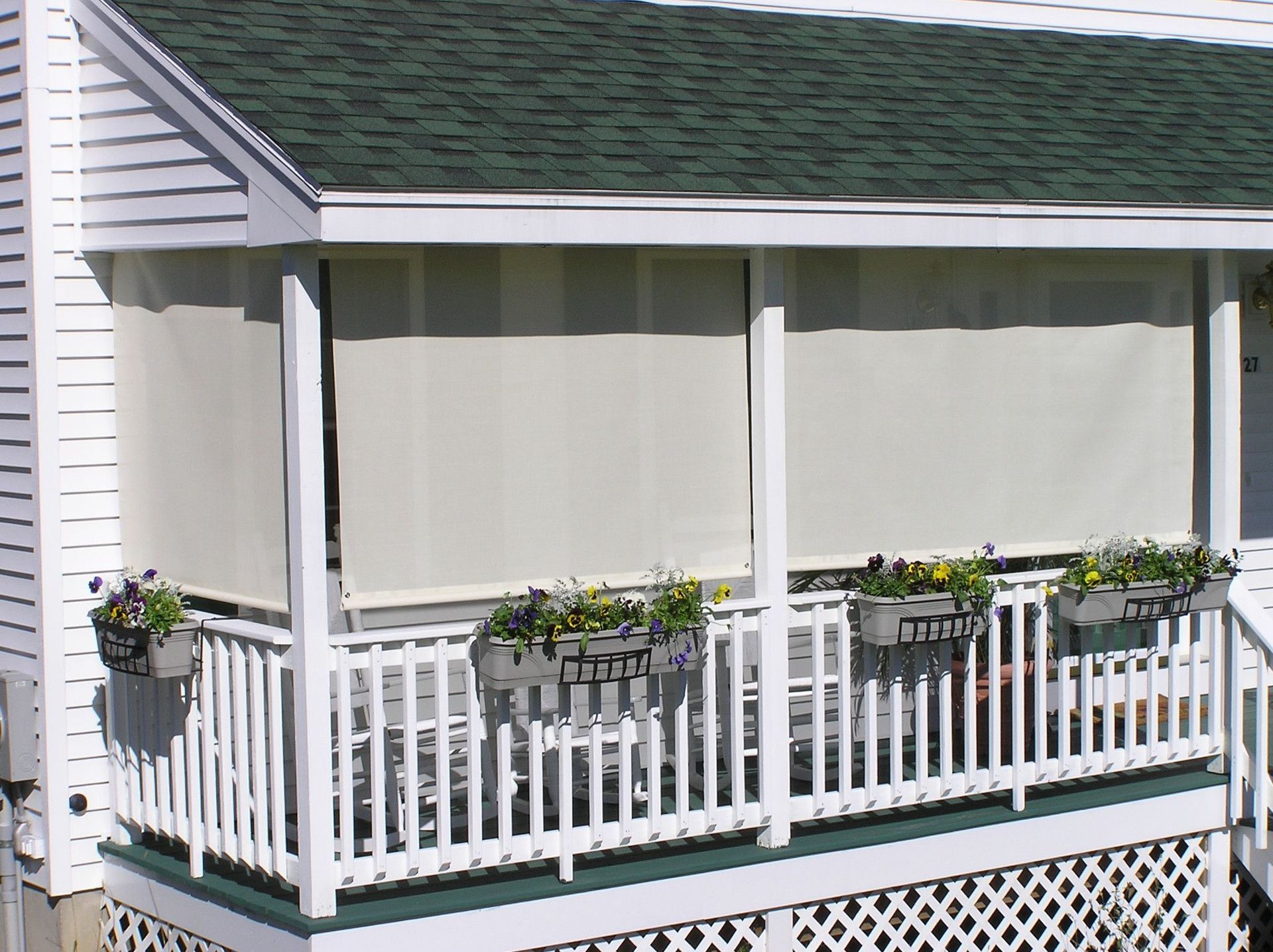 Covered porch with white siding, roll-down blinds, and flower boxes.