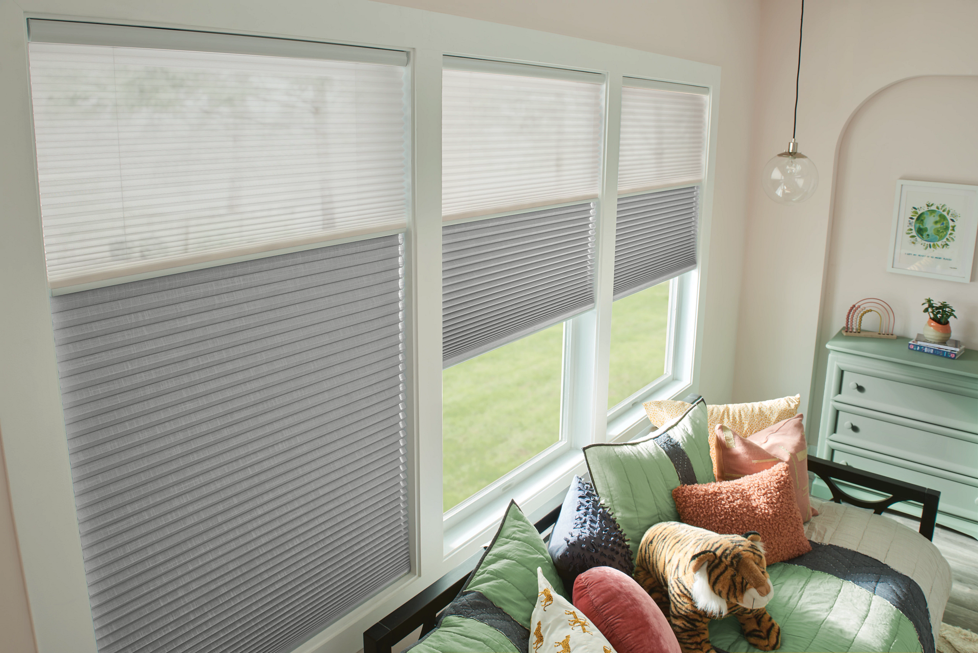 Window with light gray cellular shades, open to reveal a green yard. A bench with colorful pillows sits inside.