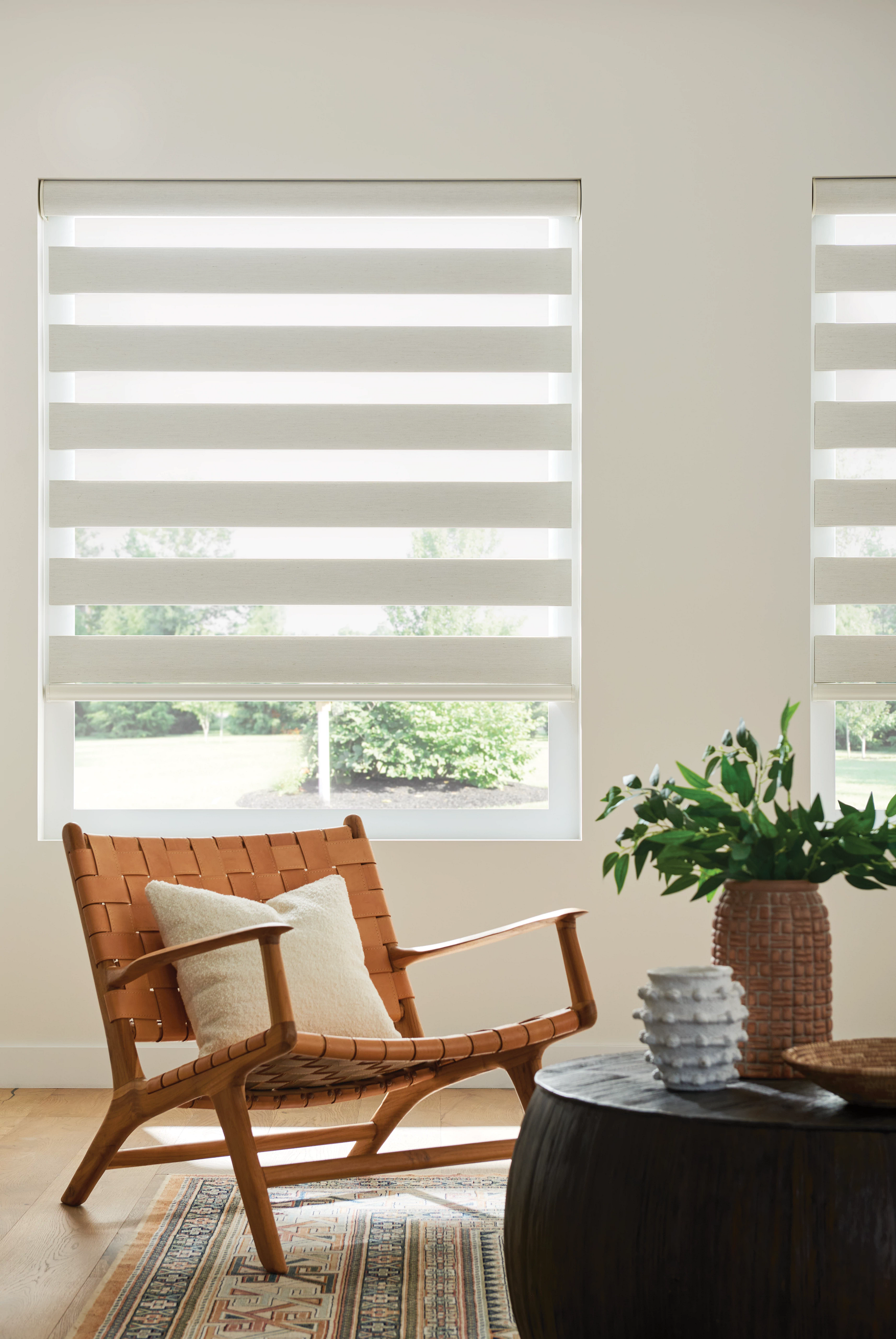 A modern living room with layered blinds, a leather chair, and a dark round table.