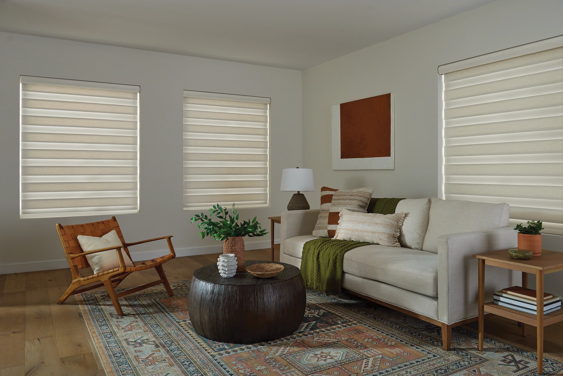 Living room with a beige sofa, wooden furniture, and patterned rug.  Beige window shades are drawn.