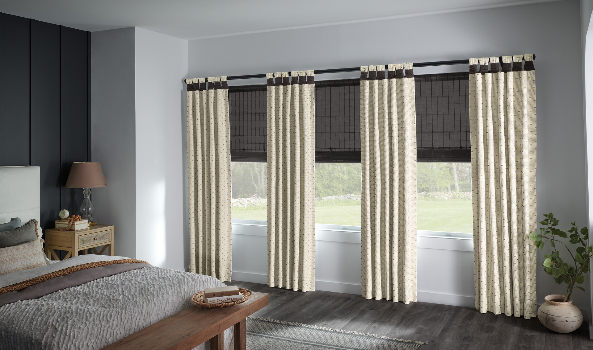 Bedroom with beige curtains, dark shades, and windows; a bed and nightstand are visible.