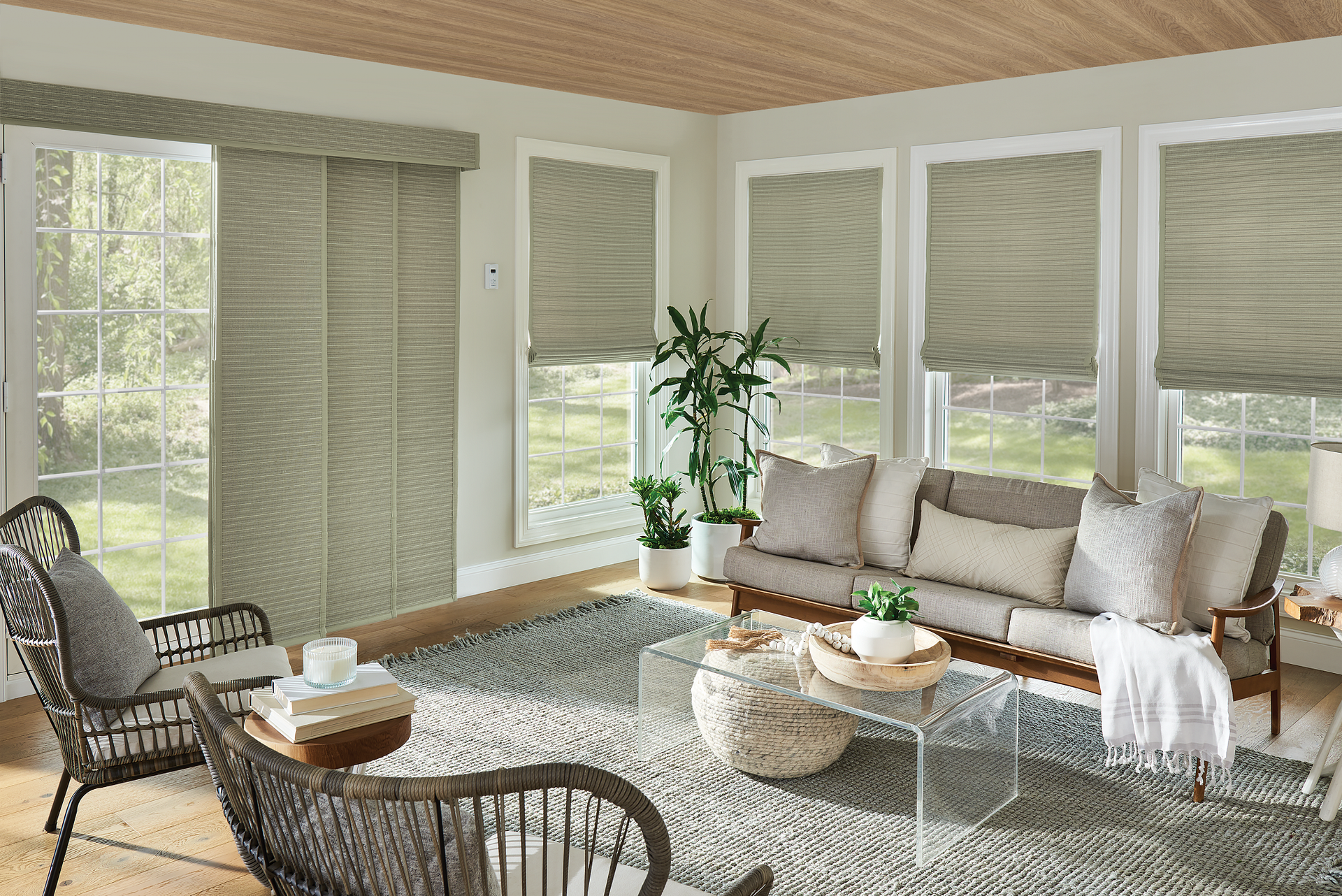 Living room with neutral tones, large windows, and woven shades. Couch, rug, and wicker furniture.