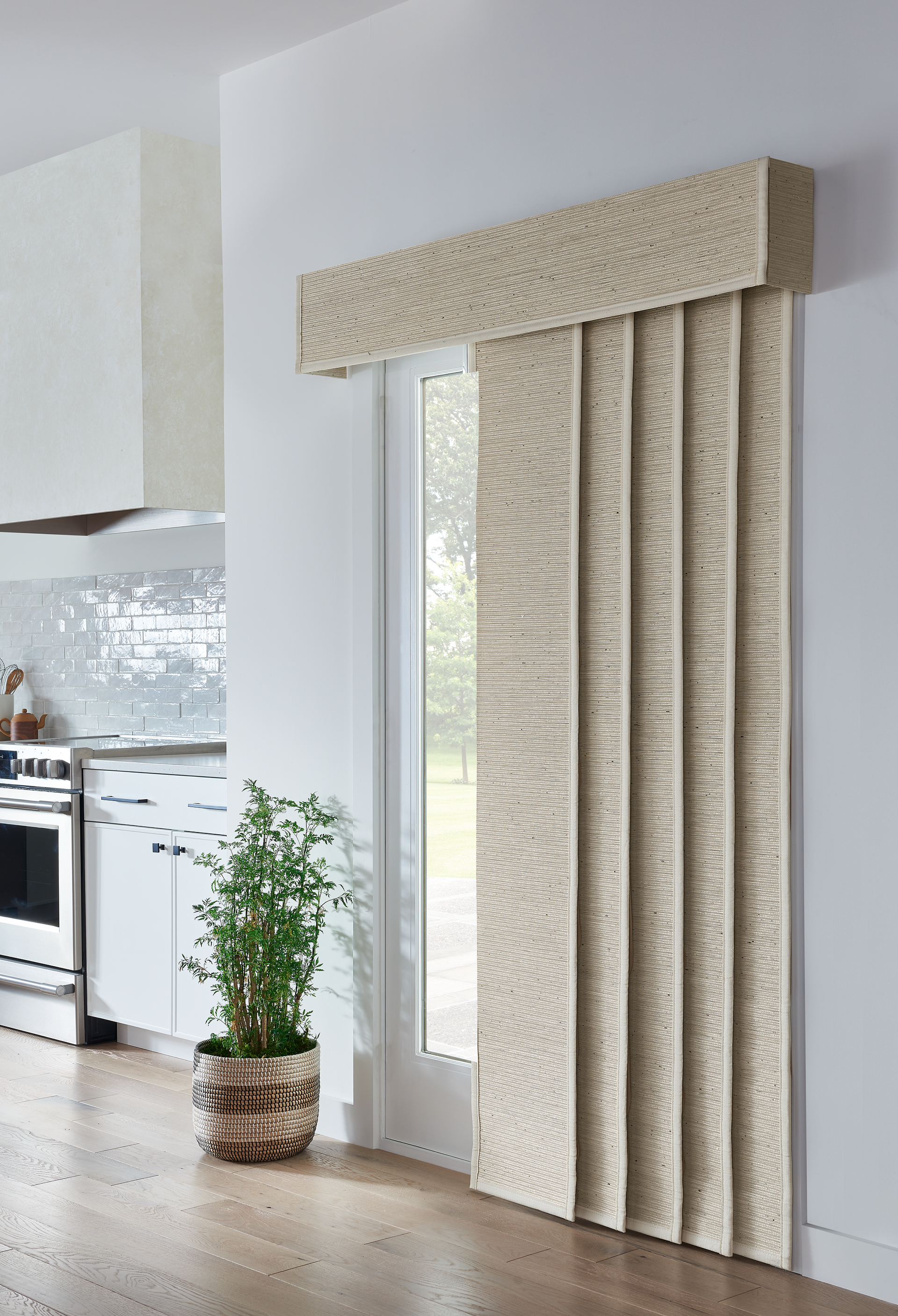 Beige textured panel blinds cover a window in a modern kitchen, over a potted plant.