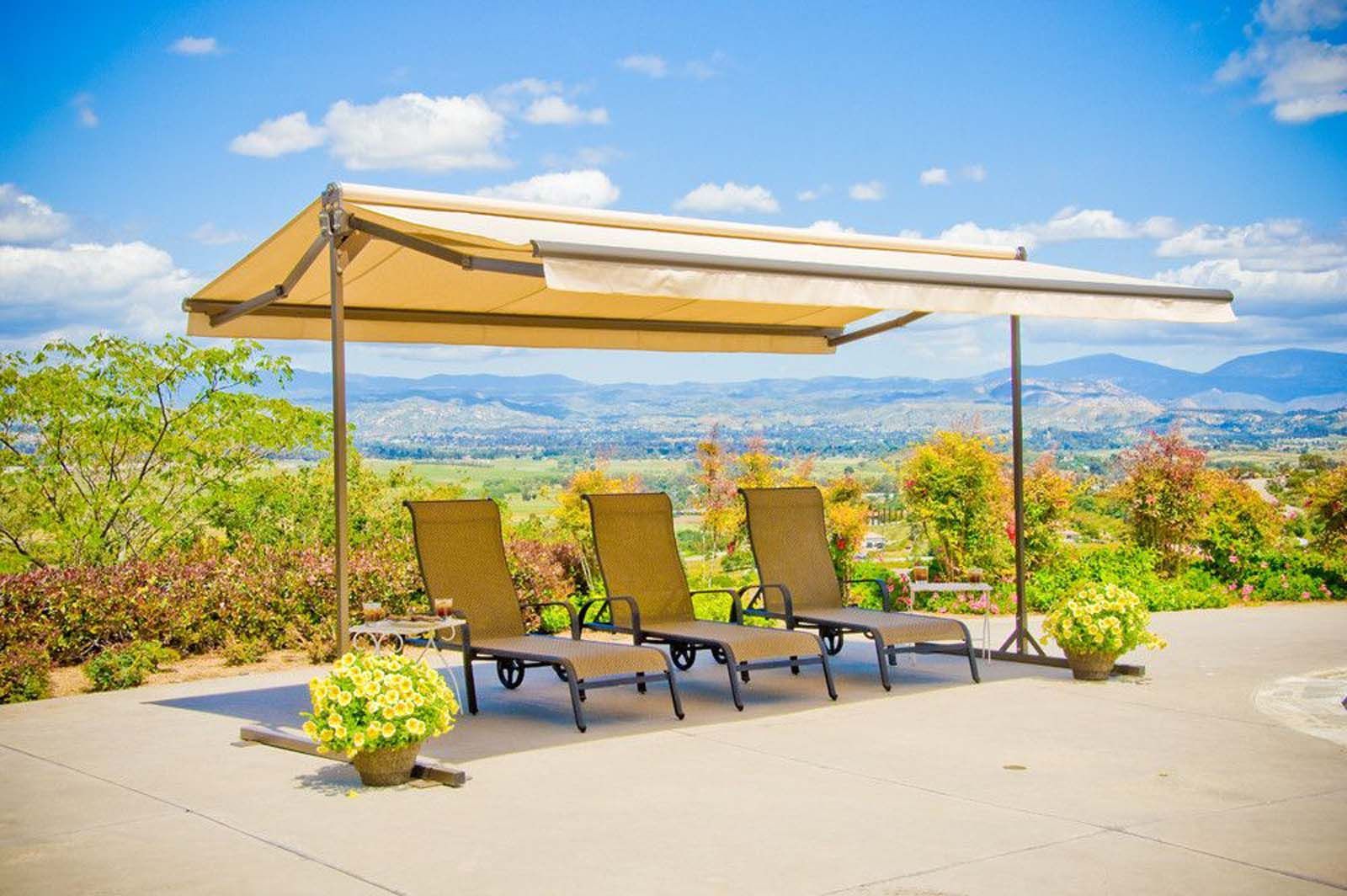 Three chaise lounge chairs under a tan canopy with a scenic mountain view.