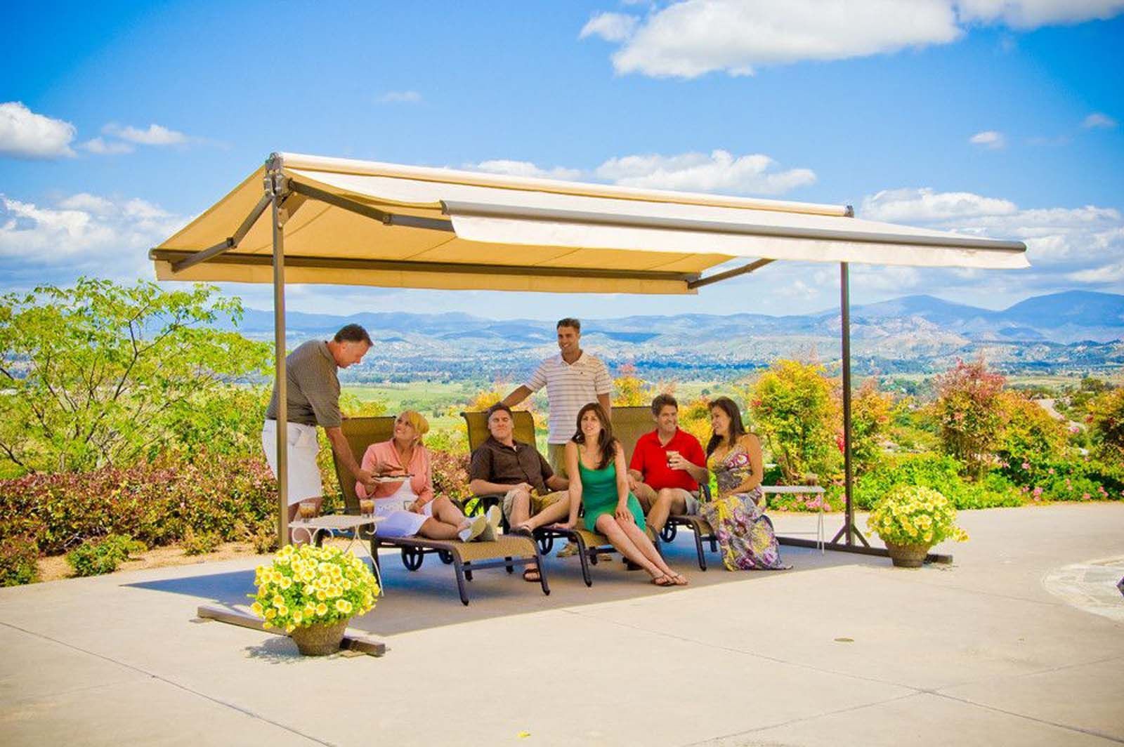 Group of people relaxing under a beige canopy, enjoying a sunny day with a scenic mountain view.