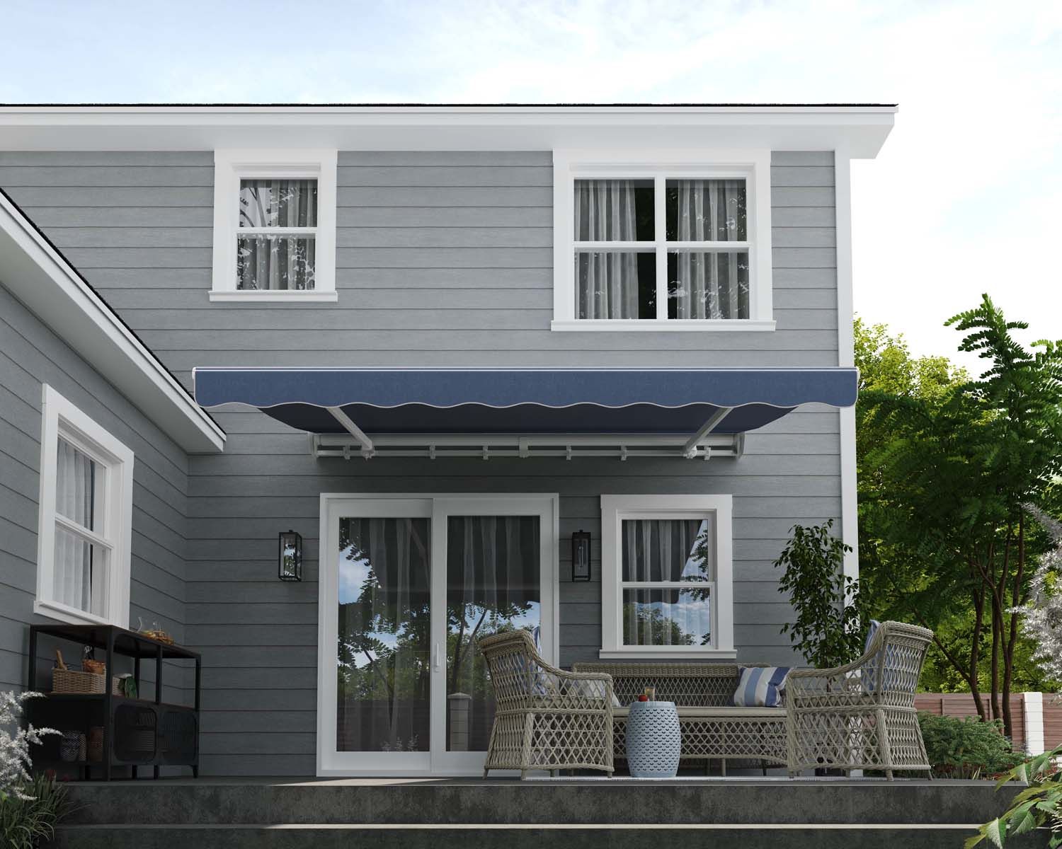 A grey house with a blue awning over a patio with wicker furniture.