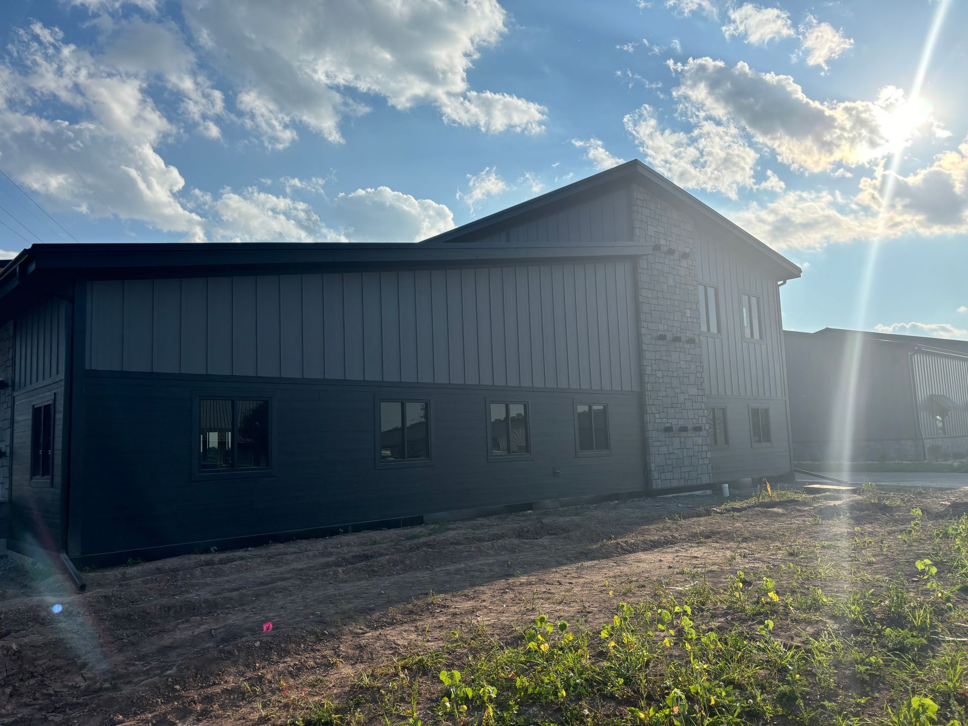 A large building is being built in a field with the sun shining through the clouds.
