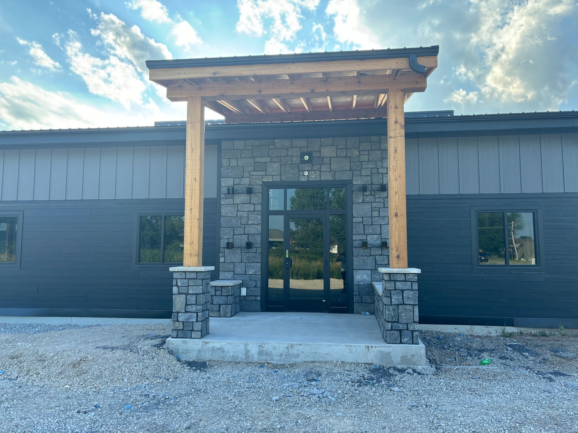 The front of a building with a wooden porch and stone pillars.
