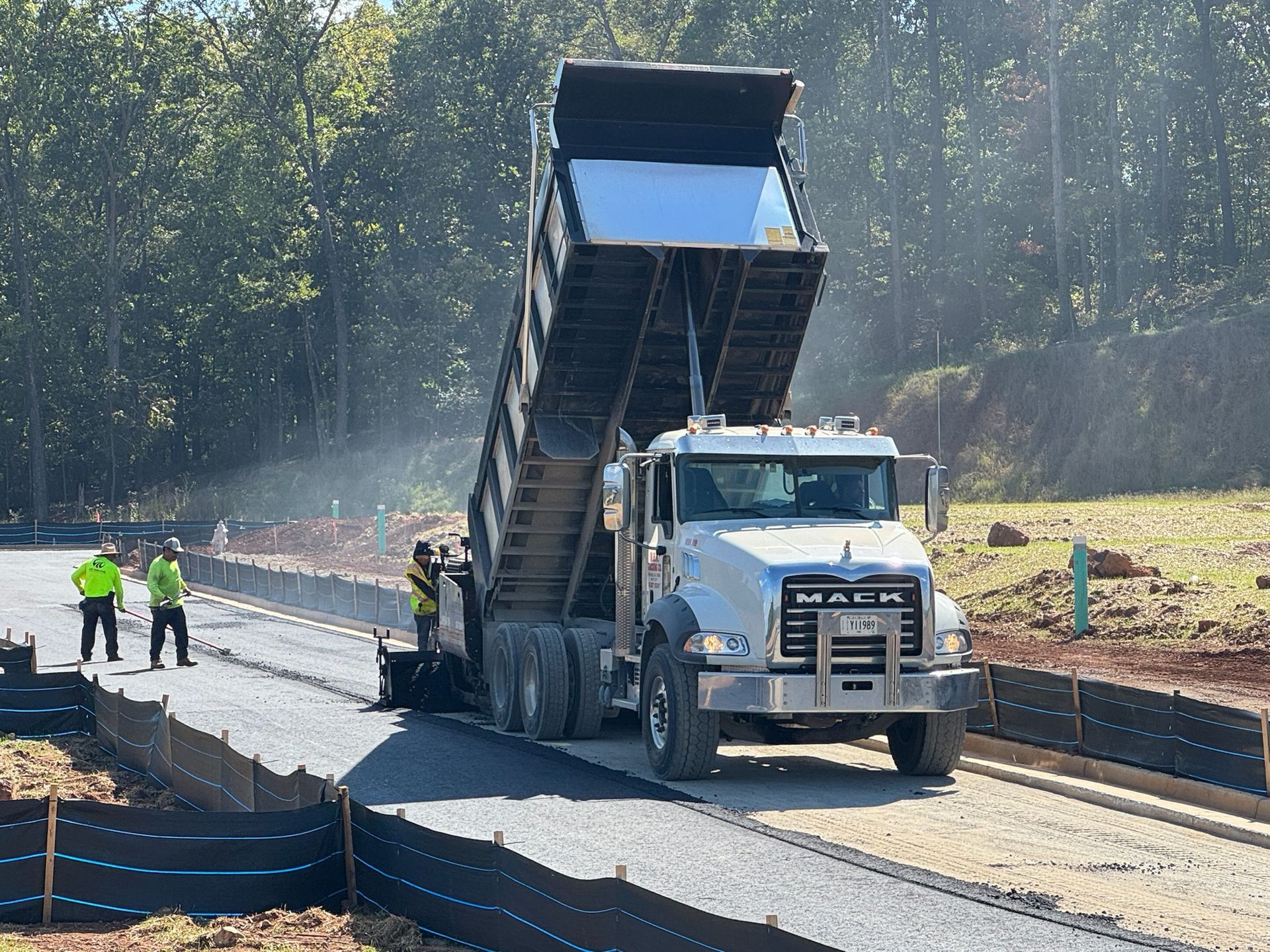 Dump truck unloading gravel on a road under construction; two workers in safety vests.