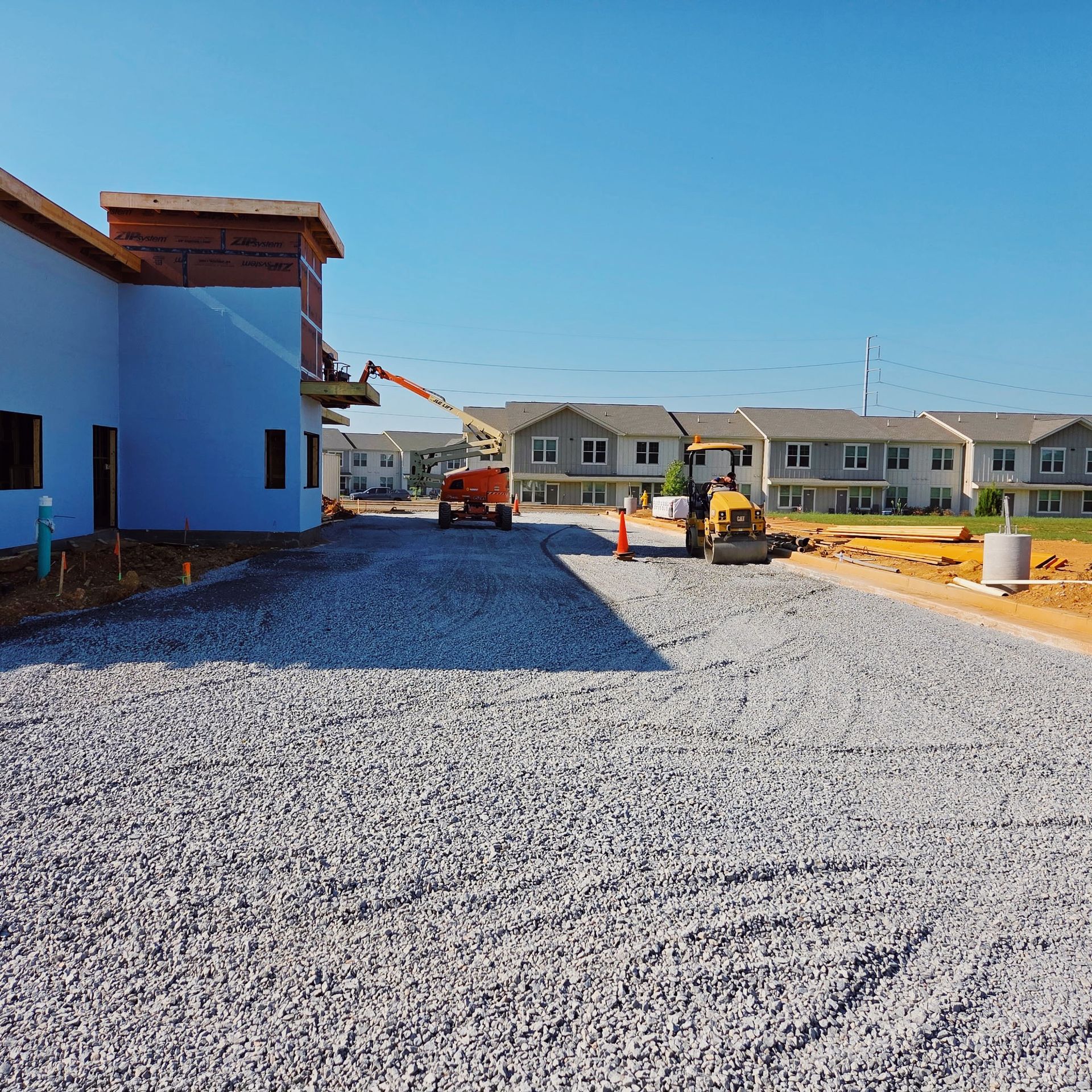 Construction site with gravel road, blue building, and heavy machinery under a bright sky.