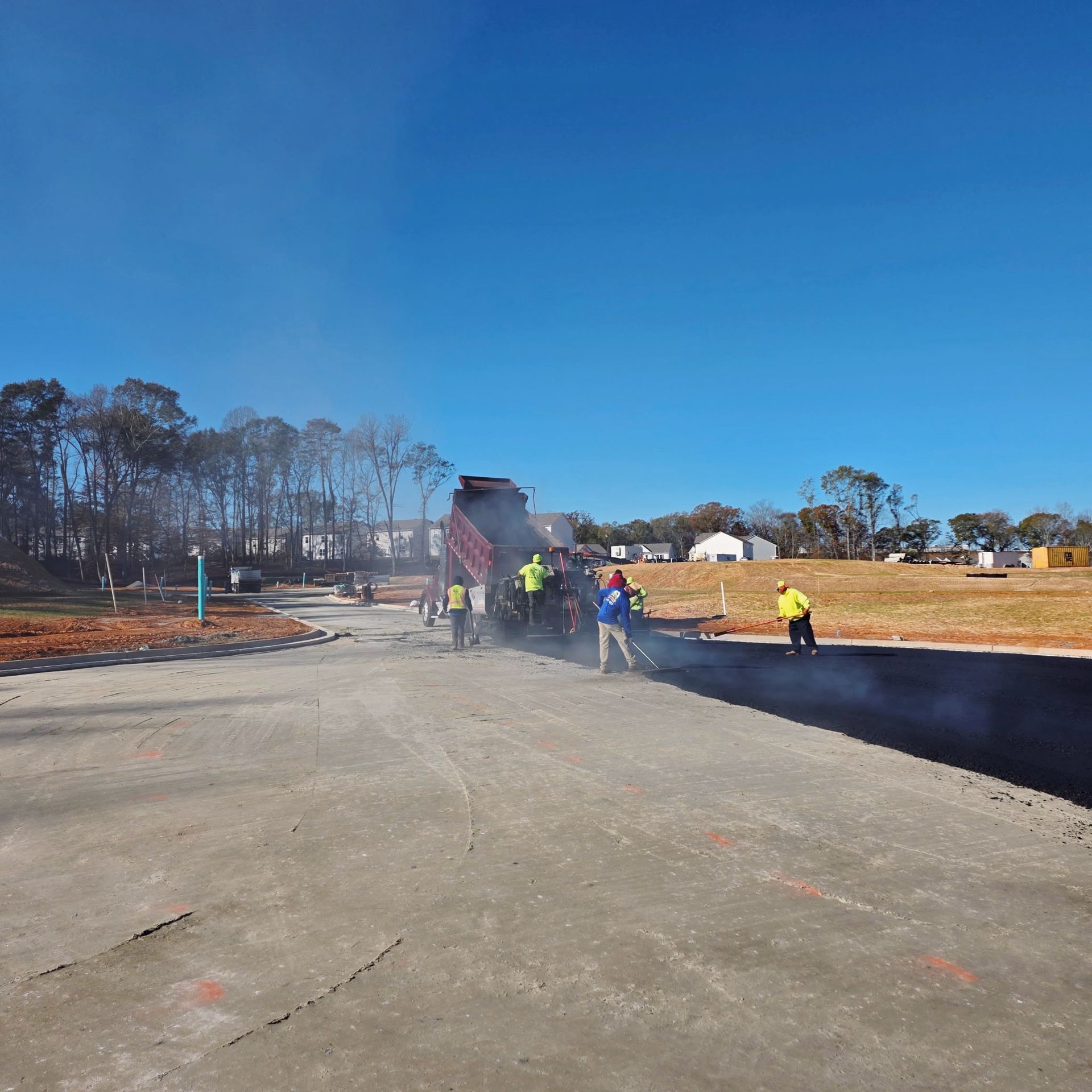 Construction workers paving a road on a sunny day. A dump truck is unloading asphalt.