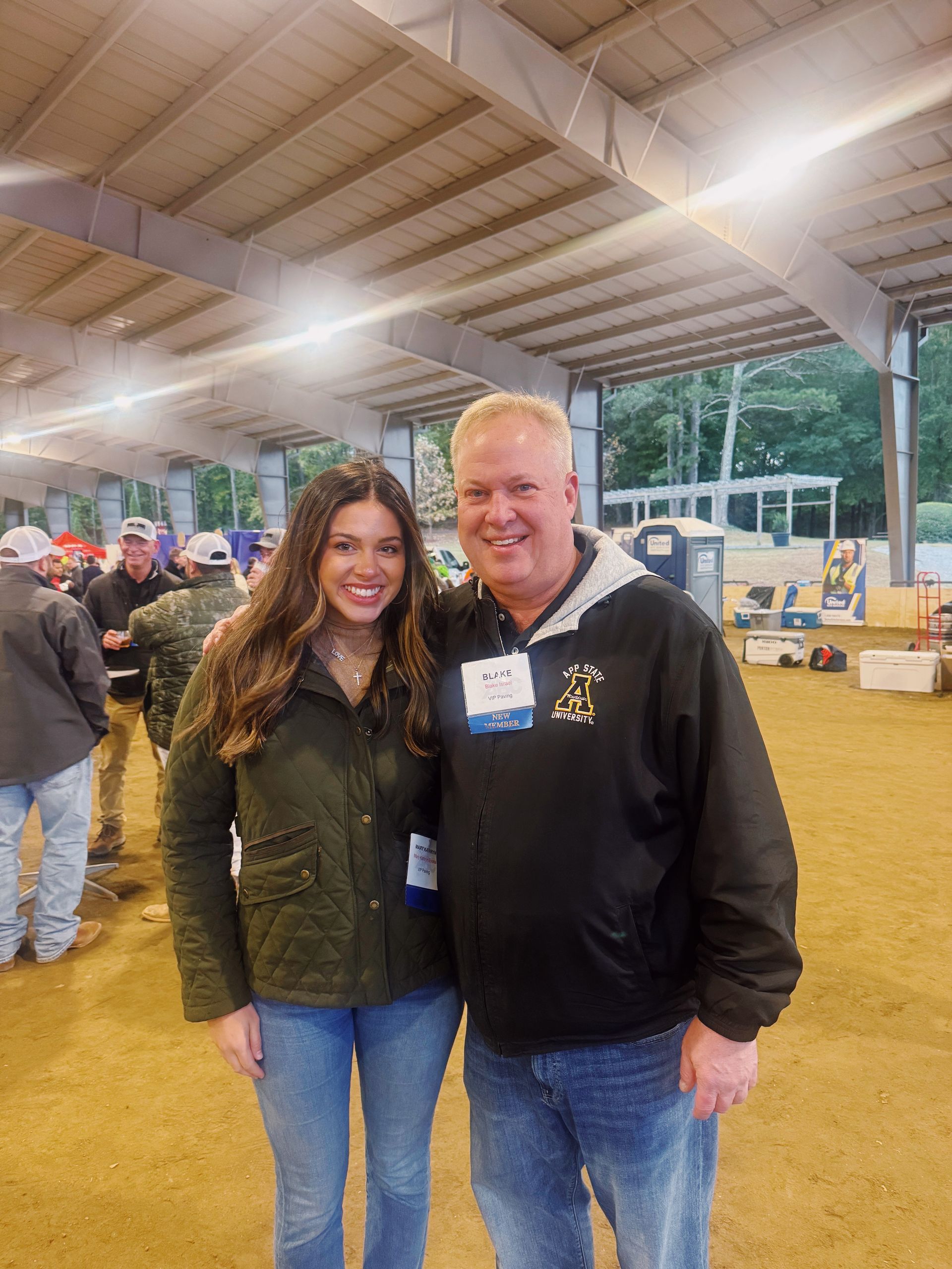 Woman and man posing together indoors, wearing casual clothing, near construction equipment.