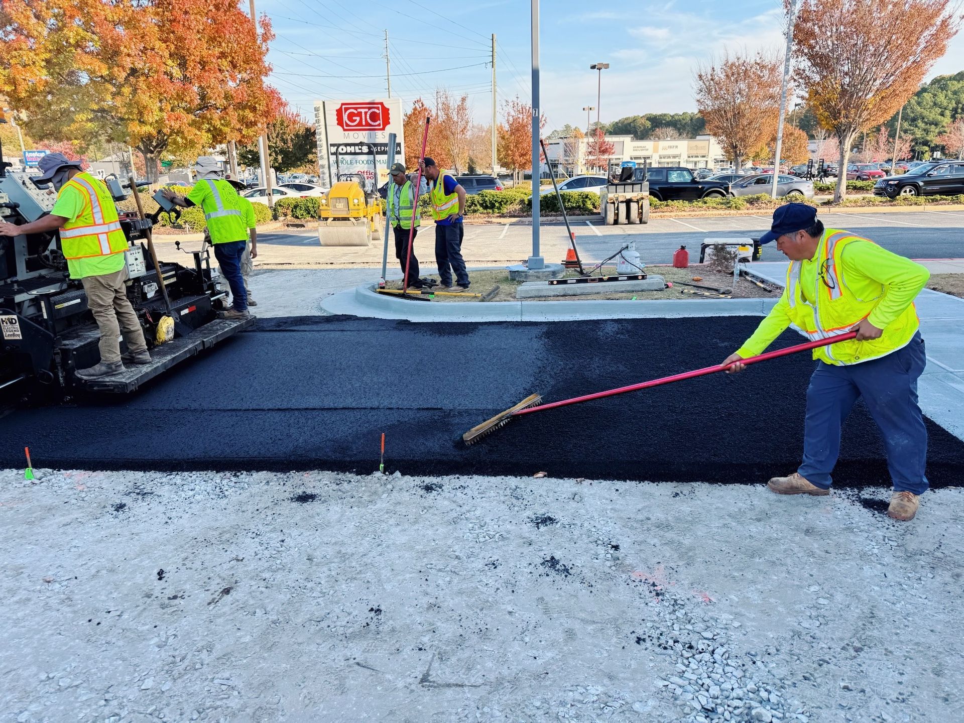Construction workers paving asphalt in a parking lot, with one worker using a rake.