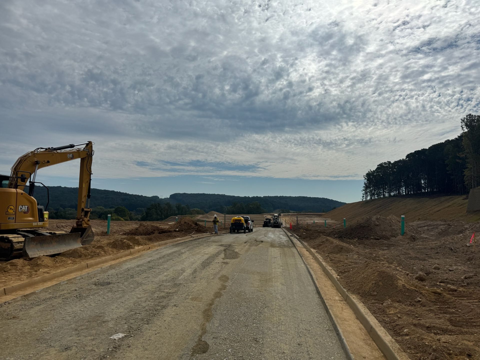 Construction site with heavy machinery, a gravel road, and cloudy sky.