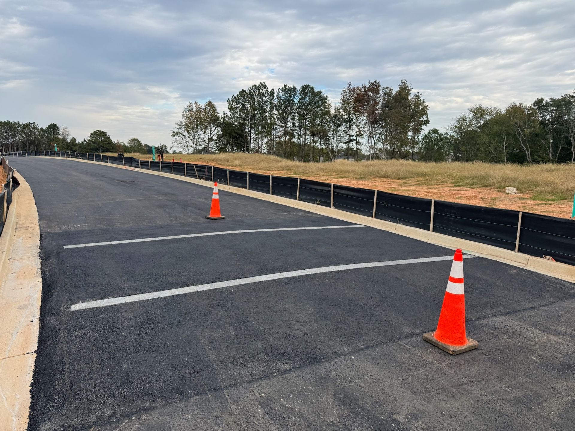 Newly paved road with orange traffic cones and black erosion barrier.