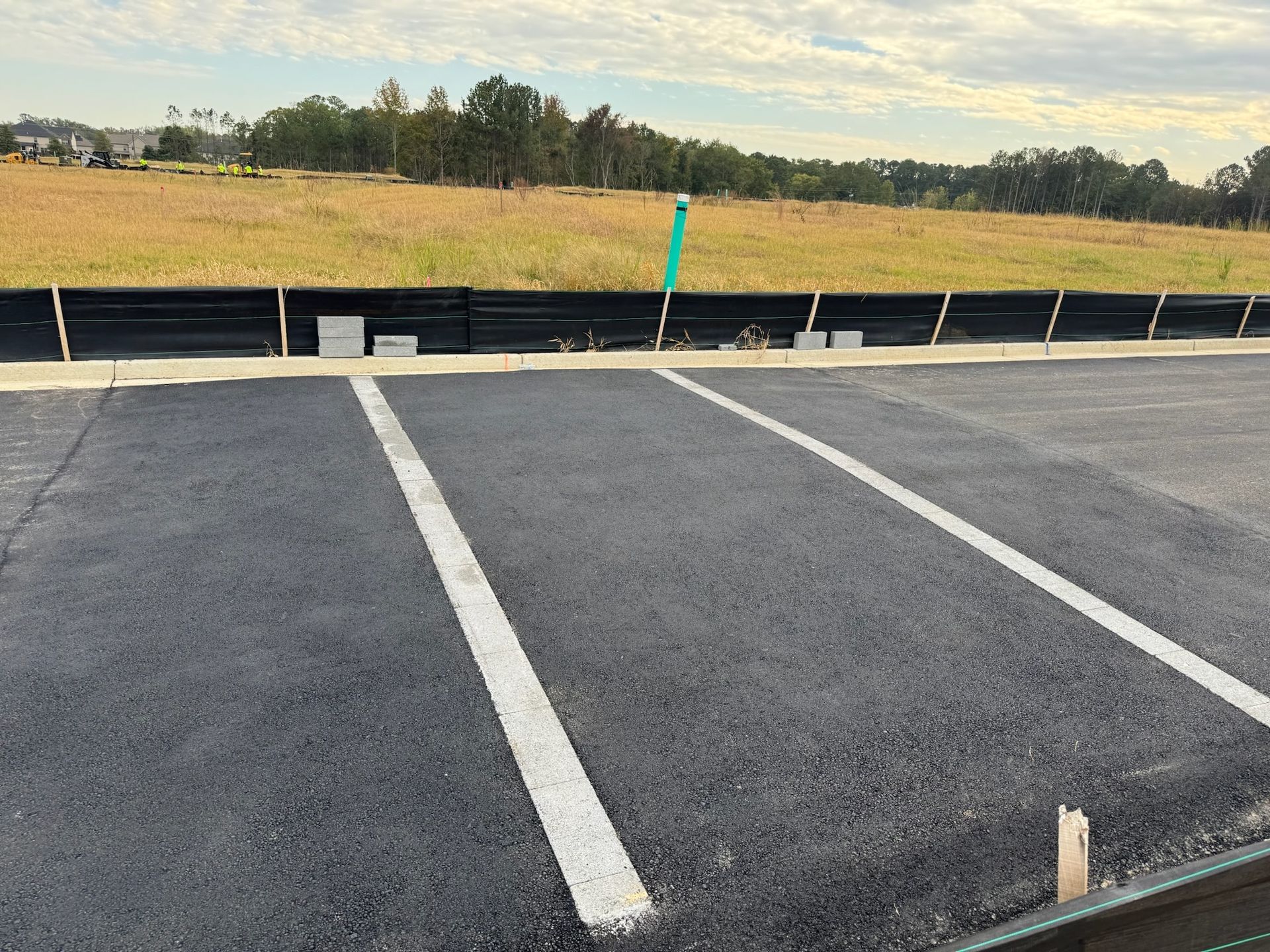 Asphalt road with white lines, backing onto a grassy field with a dark retaining wall, under a cloudy sky.