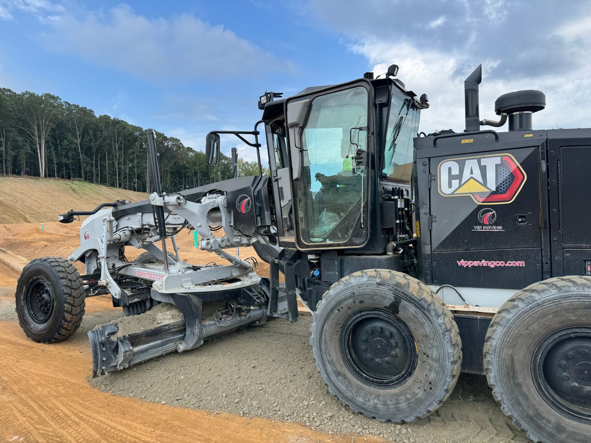 A Caterpillar grader levels gravel on a construction site.