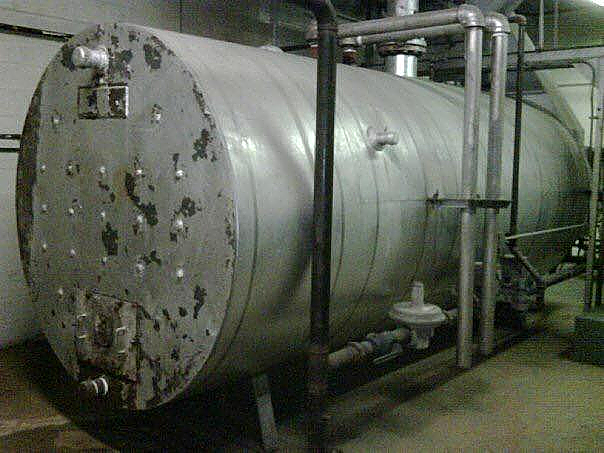 A large stainless steel tank in a room with pipes