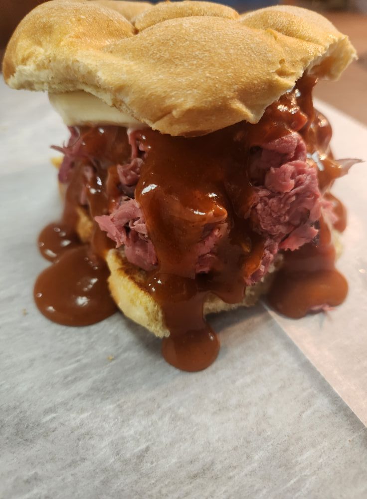 A large sandwich overflowing with meat and brown sauce on a white surface. The sandwich is on a bun.