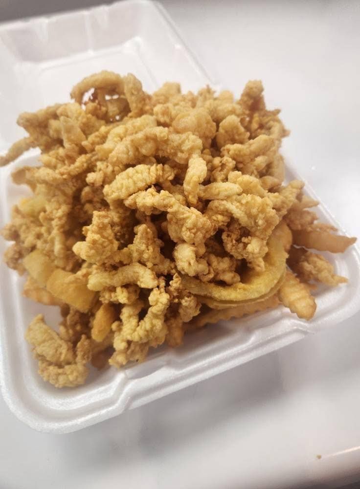 Fried clams and onion rings in a white takeout container. The food is golden brown and piled high.