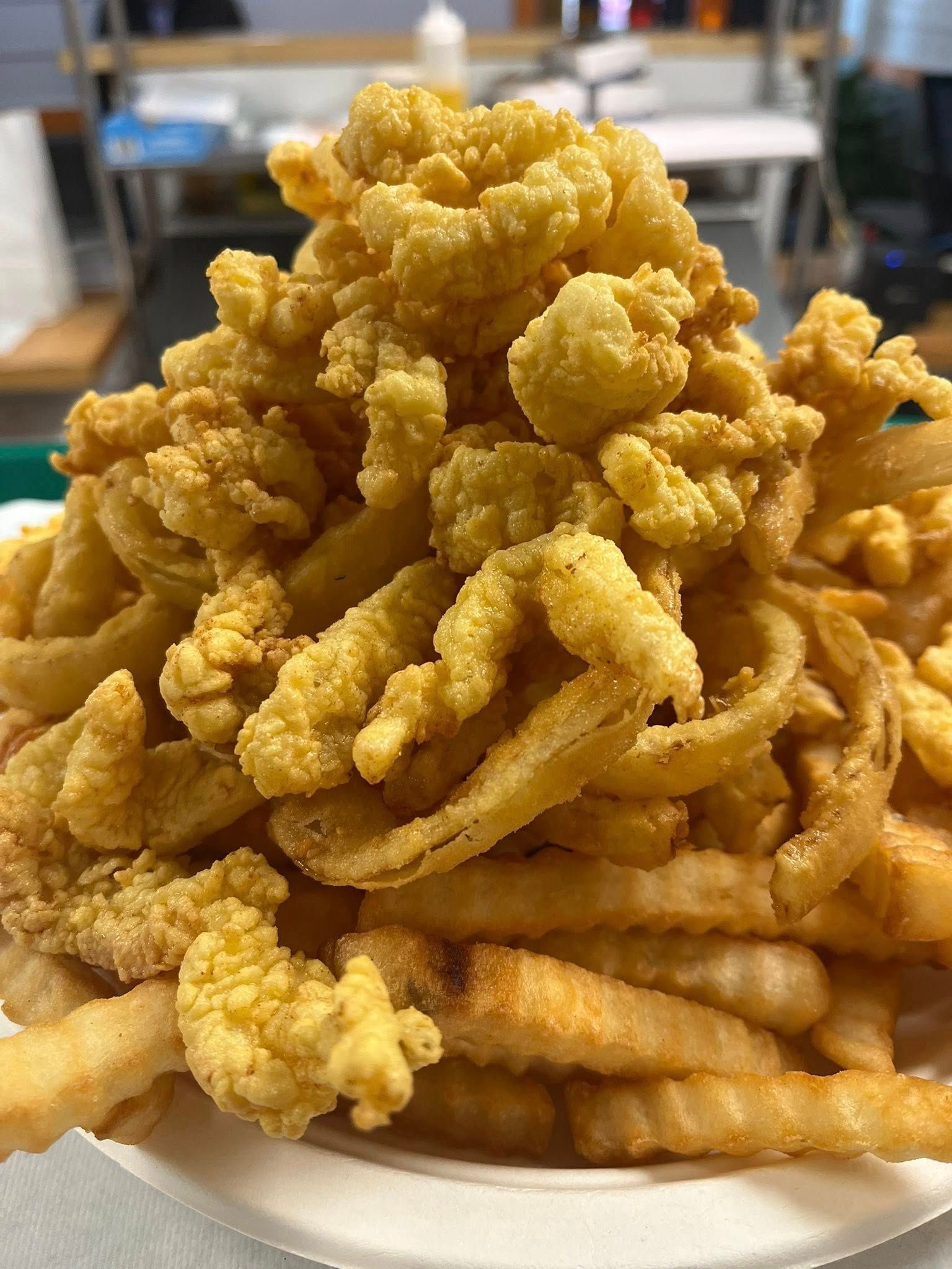 Pile of fried clams and onion rings atop a bed of french fries, served on a white plate.