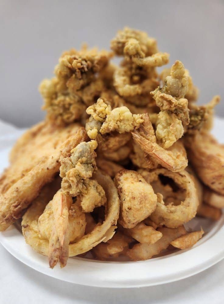 A large plate of fried seafood, including onion rings, fries, and shrimp. The food is golden brown and piled high.
