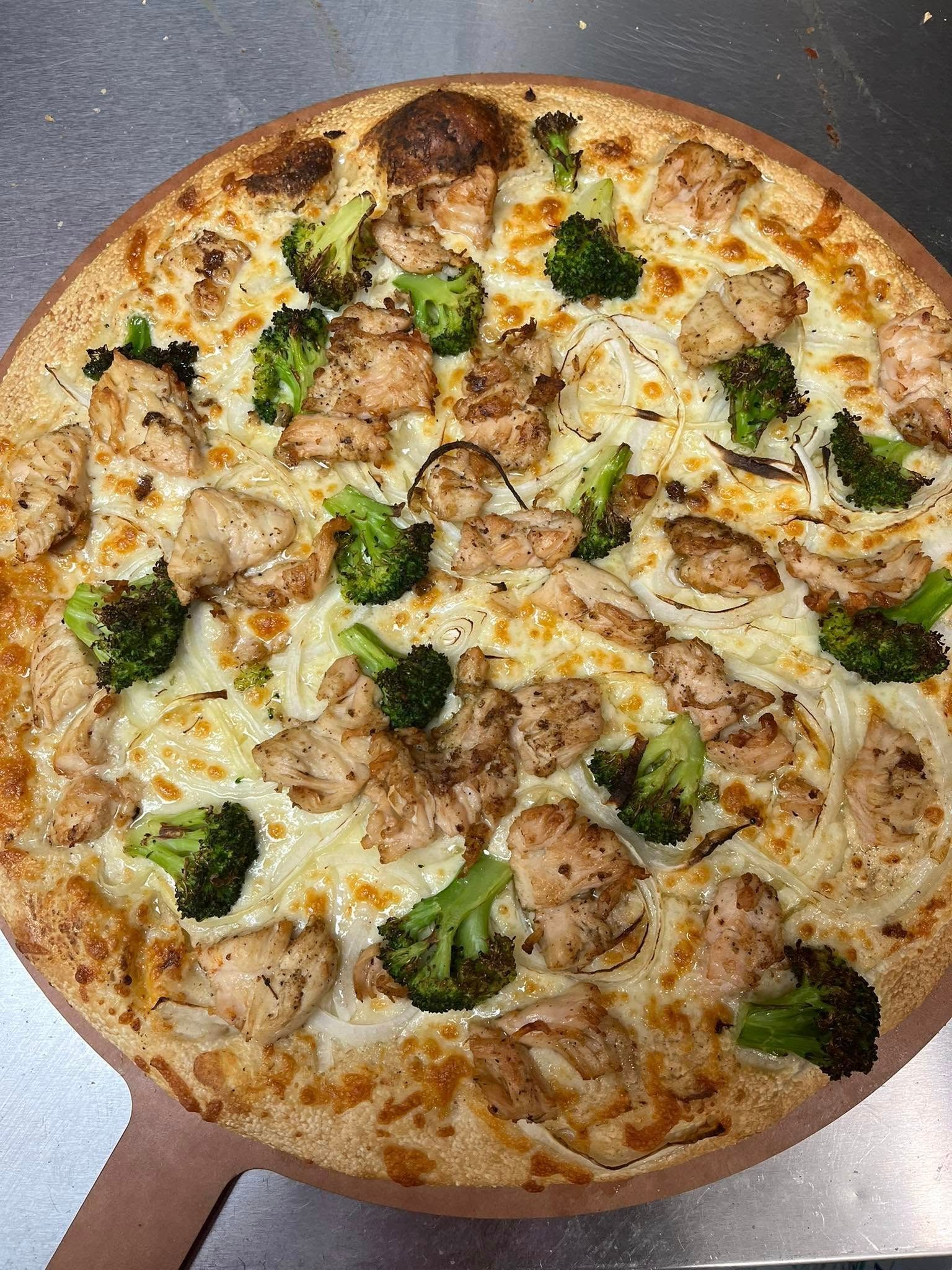 A round pizza with broccoli and chicken, baked on a wooden paddle.