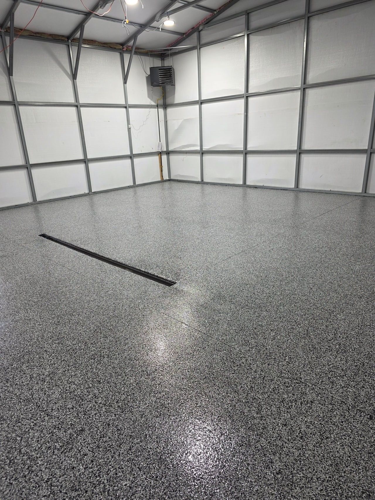Empty indoor garage with speckled epoxy floor and white paneled walls under a metal roof