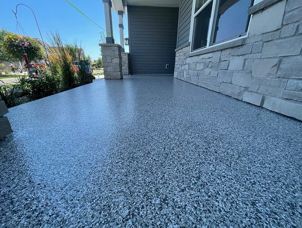 Speckled gray concrete porch beside a house with stone siding and a front entryway