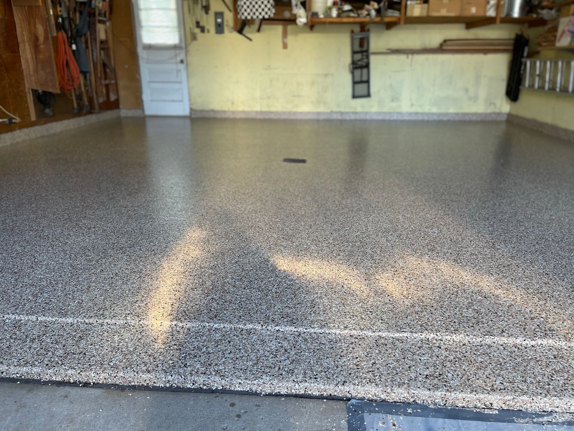 Garage floor with a speckled gray epoxy coating. The setting is a garage with tools and storage visible.
