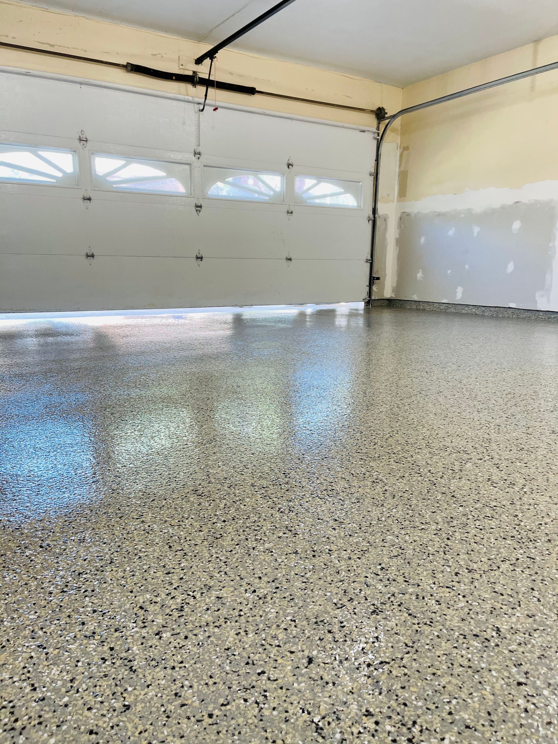 Garage interior with a speckled epoxy floor, white garage door, and pale walls.