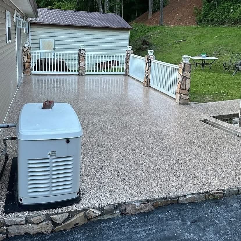A tan speckled concrete patio with a white fence and stone pillars. A generator sits on the patio. A shed and lawn are in the background.