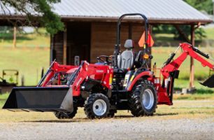 Learn More About Farm Supply Red and black tractor with front loader and backhoe in front of a wooden structure.