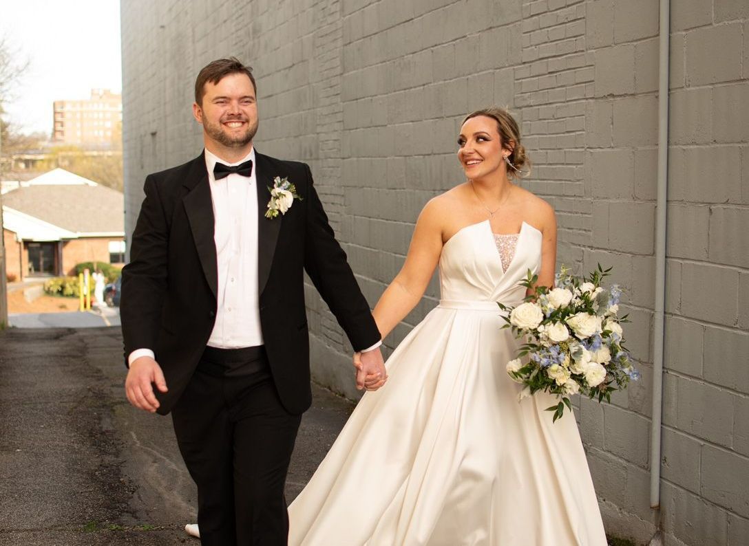 A bride and groom are walking down a street holding hands.