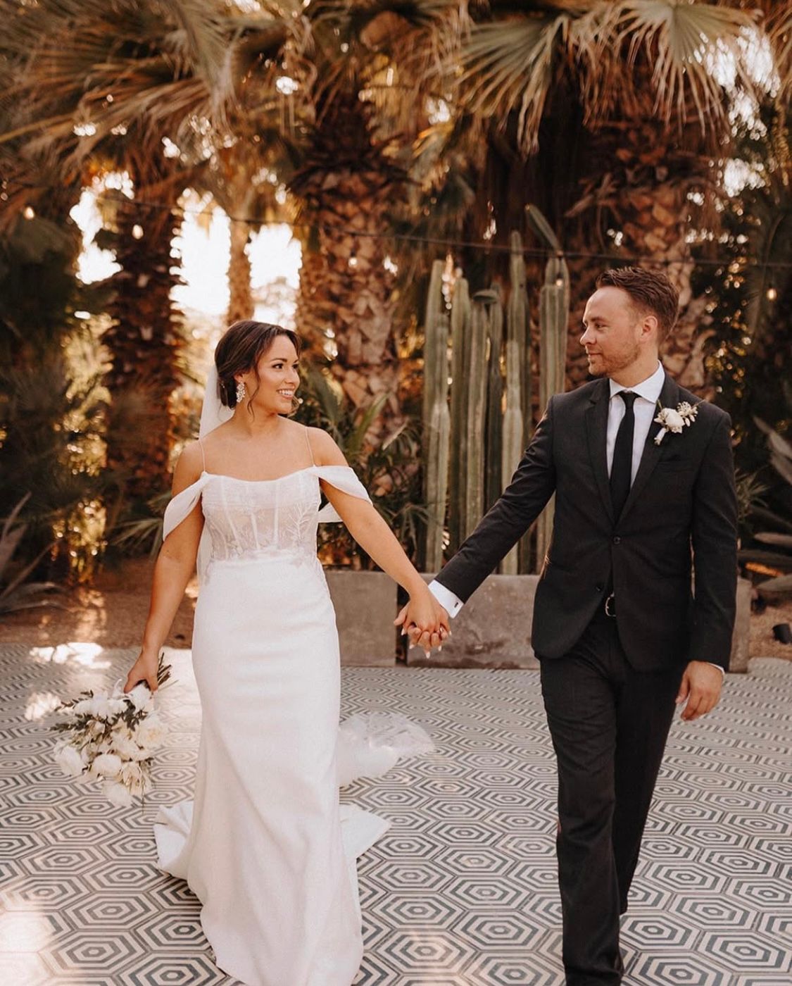 A bride and groom are holding hands while walking in the woods.