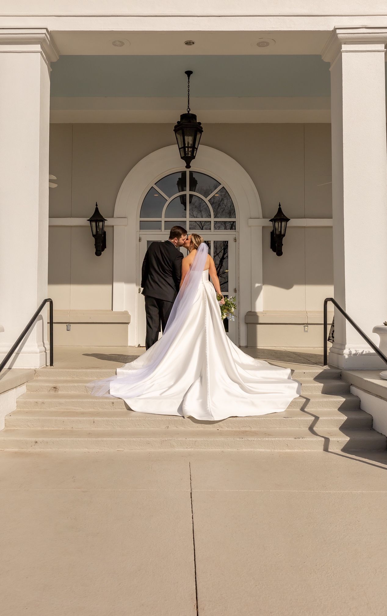A bride and groom are kissing on the steps of a building.