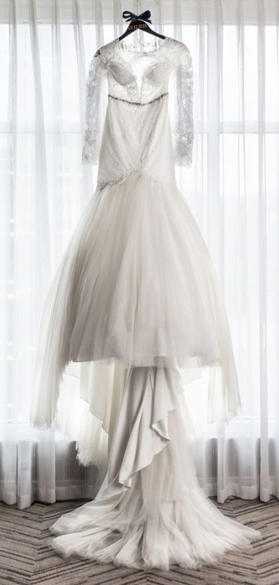 A wedding dress is hanging on a hanger in front of a window.
