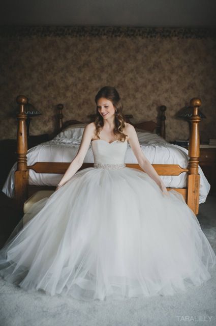 A woman in a wedding dress is sitting on a bed.