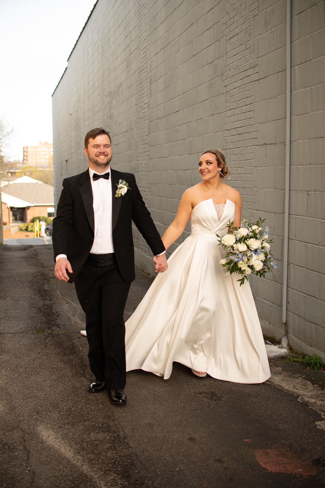 A bride and groom are walking down a street holding hands.
